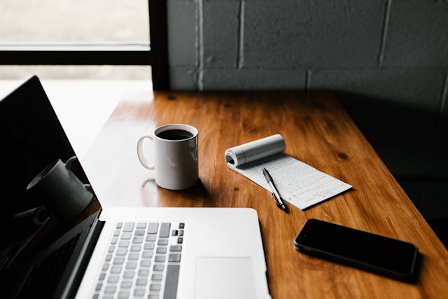 laptop with coffee and a notepad next to it