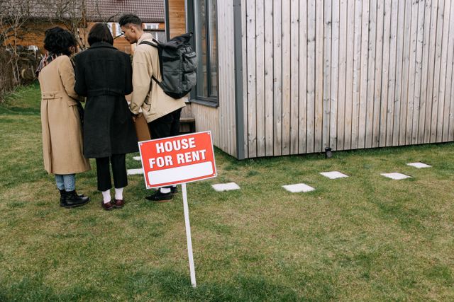people standing behind a for rent sign